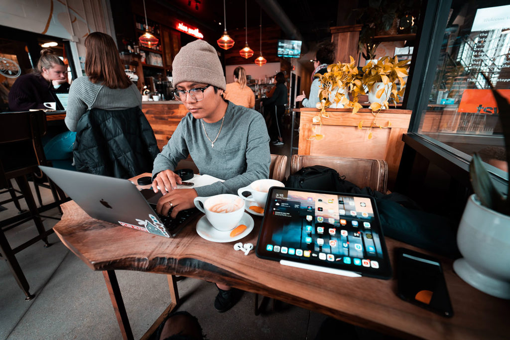 Man working in coffee shop with MacBook, iPad and coffee