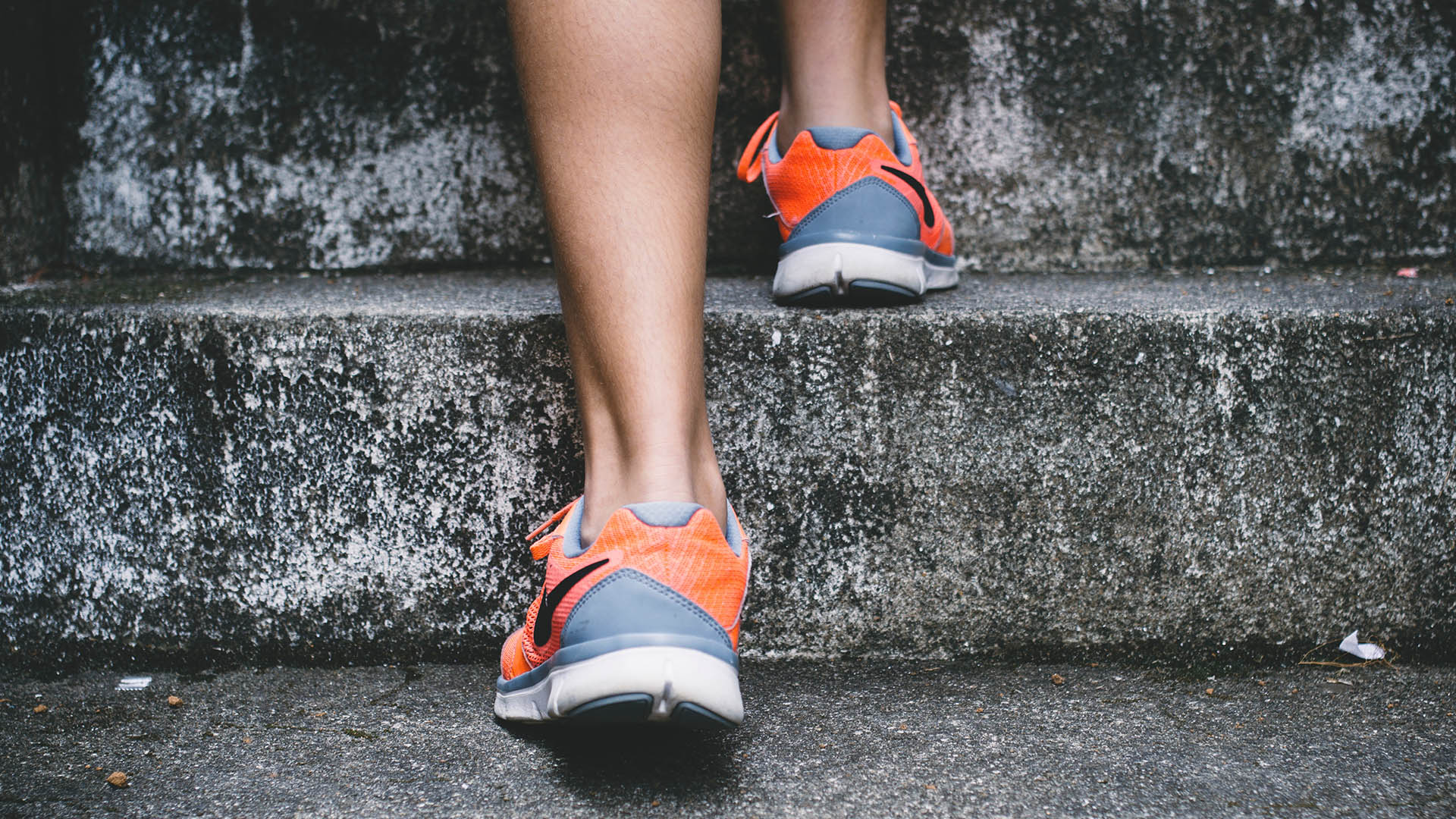 Person wearing gray and orange running shoes walking up stone stairs
