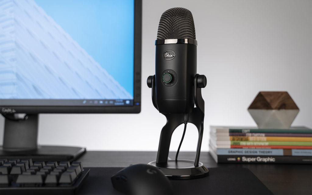 Blue Yeti X on desktop next to mouse, keyboard and screen with books laying flat in background