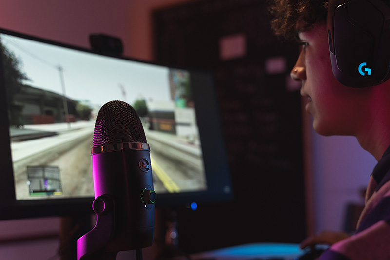 Man with Logitech gaming headhpones playing a game and recording audio with the Blue Yeti X