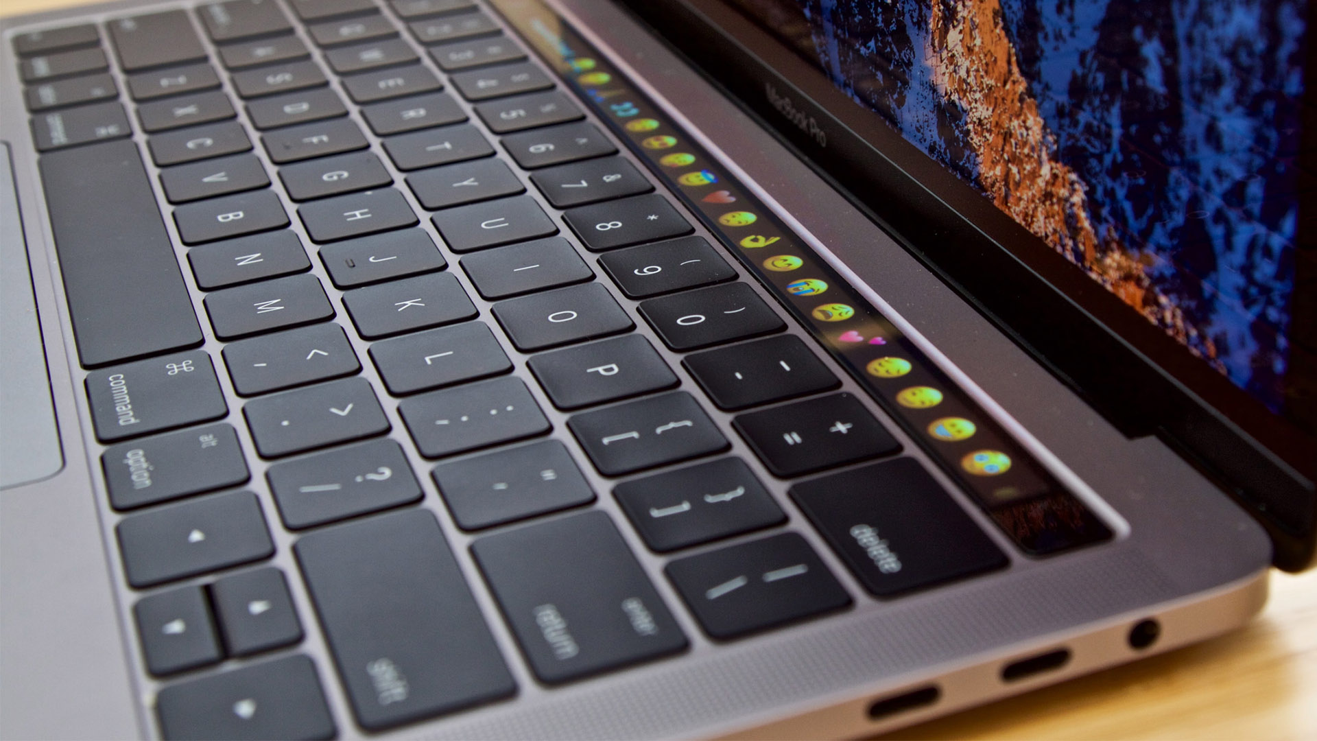 Current 13-inch MacBook Pro from right side seeing U S B C ports, keyboard and Touch Bar showing emoticons